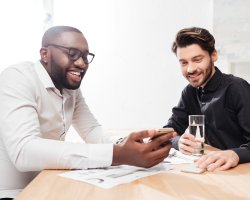 portrait-two-young-joyful-multinational-businessmen-sitting-table-happily-talking-while-working-together-office-isolated portrait-two-young-joyful-multinational-businessmen-sitting-table-happily-talking-while-working-together-office-isolated